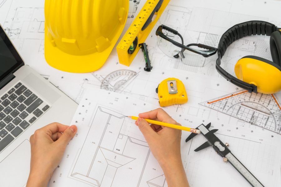 Hand over Construction plans with yellow helmet and drawing tool Hand over Construction plans with yellow helmet and drawing tools on blueprints